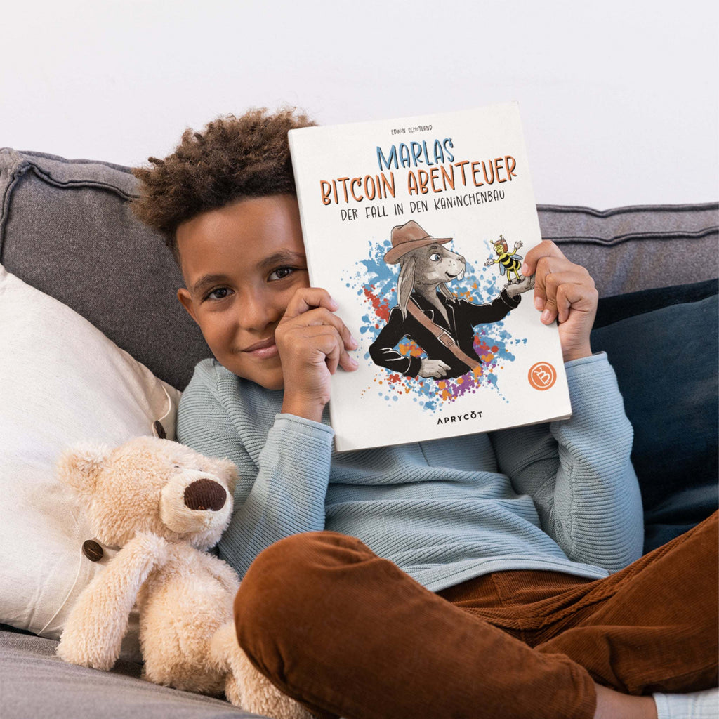 Kind sitzt auf einem Sofa und hält „Marlas Bitcoin Abenteuer“ vors Gesicht
